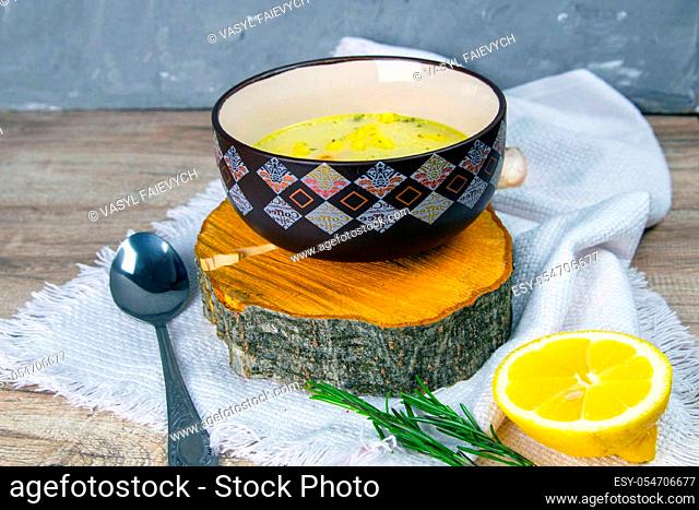 Potato cream soup with mushrooms, carrots and cheese. Top view. Soup in a brown plate, stands on a wooden stand, next to a hour, spoon, spices and lemon