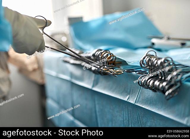 Doctor in medical glove is taking a surgical forceps from the table in the operating room. Closeup low aperture photo. Horizontal