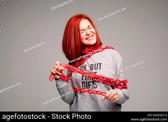 Studio portrait of a girl entangled in a chain. A red-haired woman with brown hair tries to get rid of the chain. The concept of a life-like situation