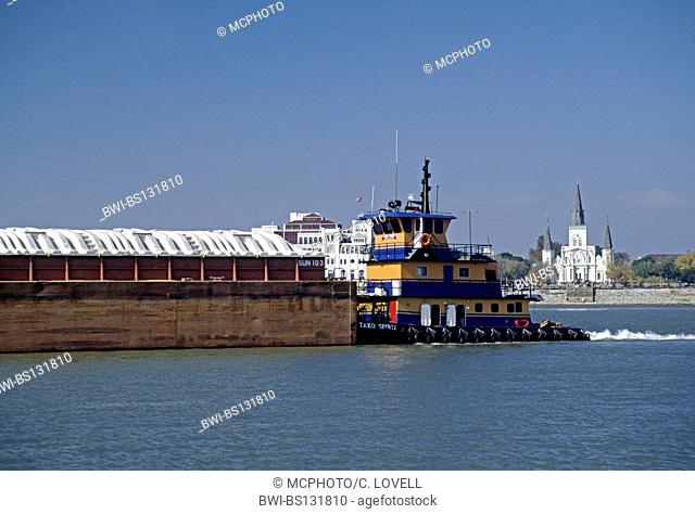 A tugboat pushes a barge along the Mississippi River as it winds past St. Louis Cathedral in the FRENCH QUARTER, USA, Louisiana, New Orleans