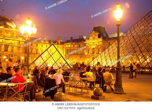 Sitting in a cafe in Cour Napoleon by the Pyramide and Musee du Louvre in Paris at night, France
