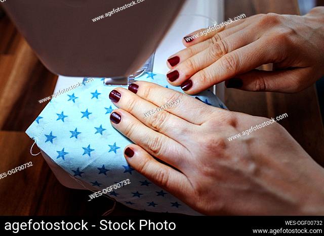 Woman's hand stitching mask on sewing machine at home