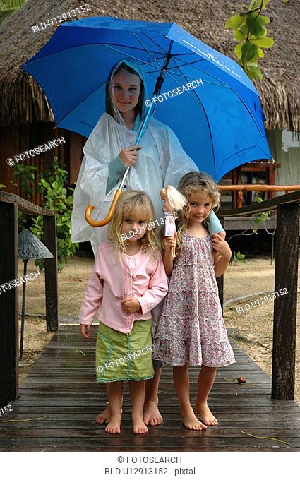 A young mother holding an umbrella standing with her two young daughters