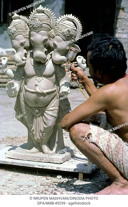 man doing spray painting on Lord Ganesh ganpati statue