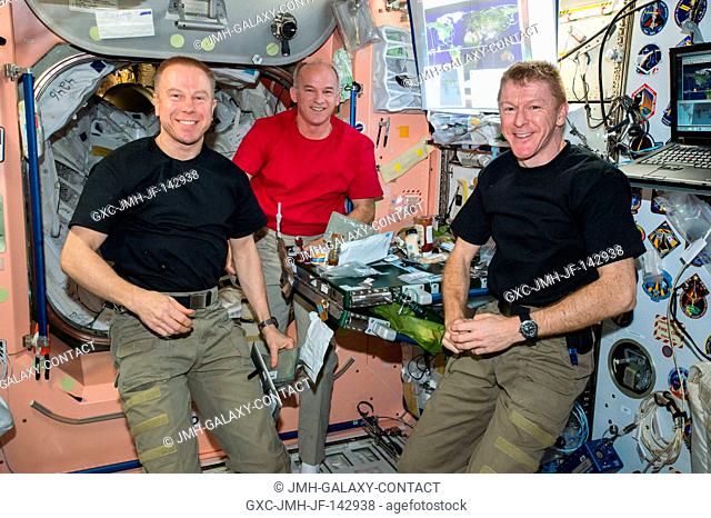 Expedition 47 crew members Tim Kopra (left), Jeff Williams (center) Tim Peake (right) are seen eating dinner inside the Unity module aboard the International...