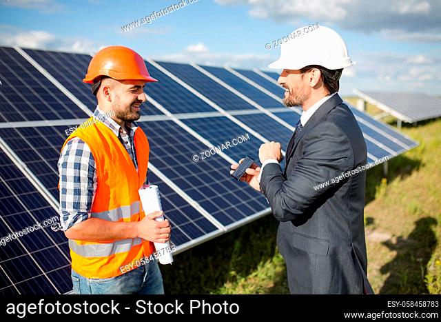 Business client showing photovoltaic detail to foreman. Solar energy station in the field, worker ond order comminicating