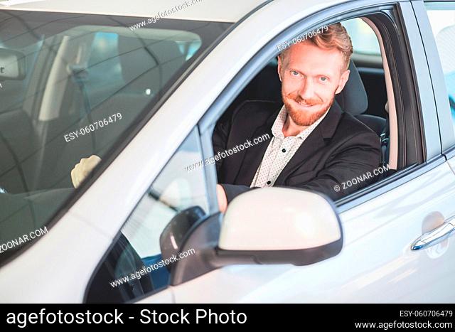 Happy man buying new car in auto showroom. Smiling man sitting in new car
