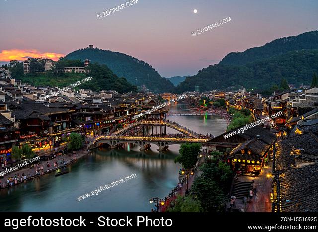 Feng Huang, China - August 2019 : Illuminated at night old historic arched Xueqiao Snow Bridge on the riverbanks of Tuo river