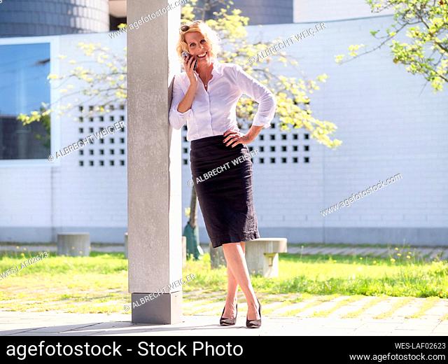 Smiling businesswoman talking over smart phone while standing by column