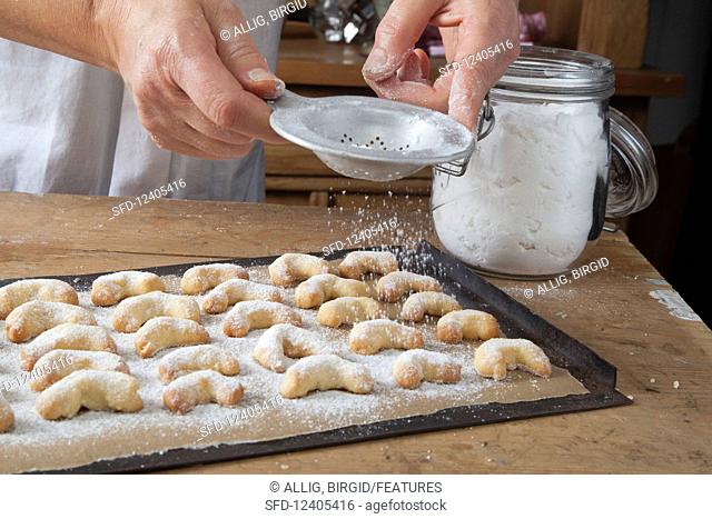 Gluten-free vanilla crescent biscuits being dusted with icing sugar