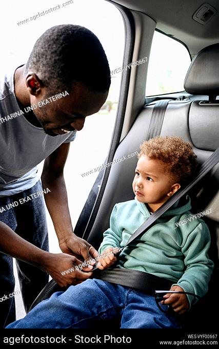 Father adjusting seat belt of daughter sitting in car