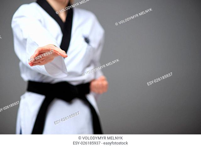 The hand of karate girl in white kimono and black belt training karate over gray background