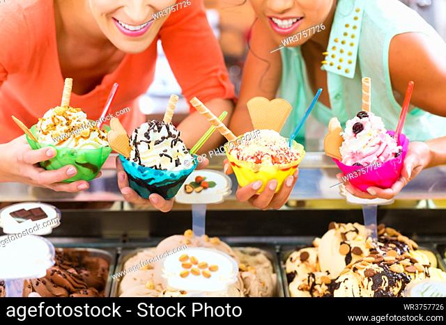 Young female customers or friends with sorts of ice cream for cornets and cones and sundaes in parlor