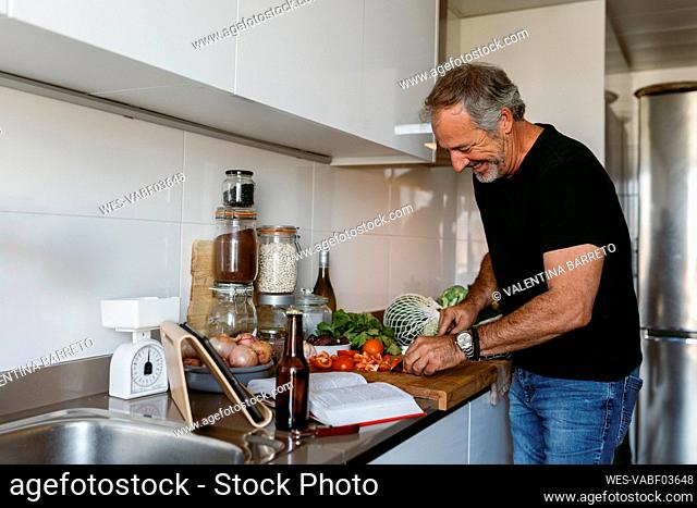 Smiling mature man cutting vegetable while standing in kitchen at home