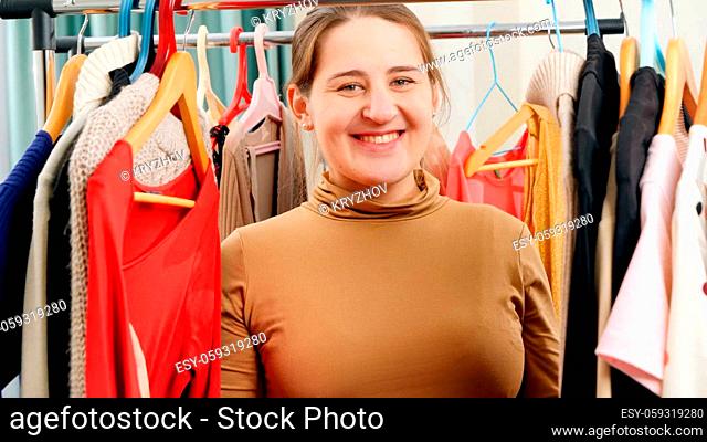 Portrait of beautiful elegant woman posing in big wardrobe and looking through clothes on hangers on clothes rack