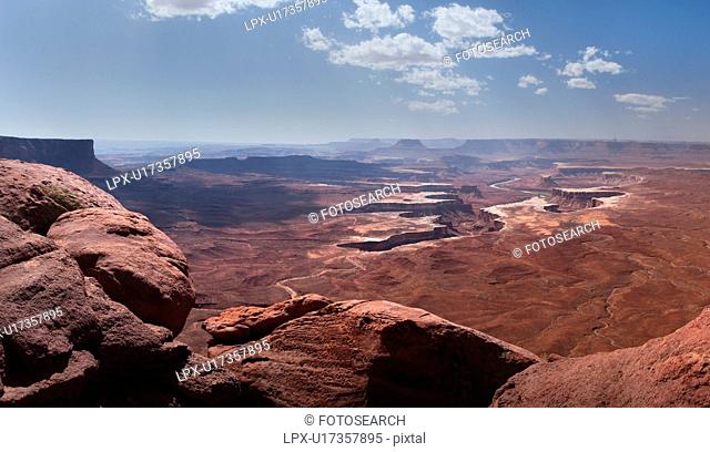 Panorama view of Green River Overlook, stretching miles to deep winding crevice in valley, sunny fall morning, with blue sky and puffy cloud formation, Utah