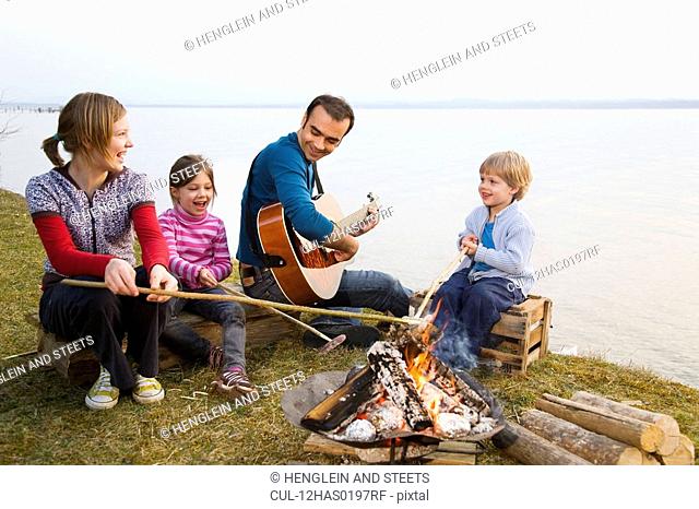 two girls, boy and man roasting sausages