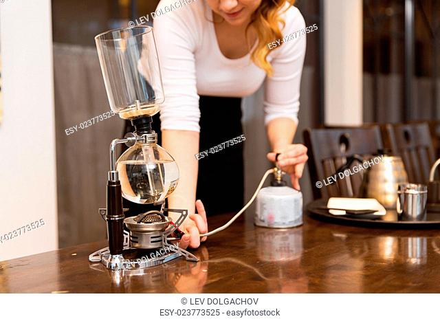 equipment, coffee shop, people and technology concept - close up of woman with butane gas burner heating water in siphon coffeemaker at cafe bar or restaurant...