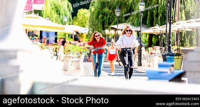 Trendy fashinable teenager girls riding public rental electric scooters in urban city environment. New eco-friendly modern public city transport in Ljubljana