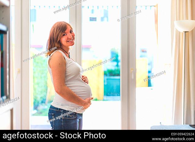 Happy Caucasian pregnant mother touching her tummy, blue jeans, close up