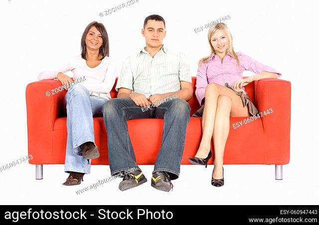 Smiling man and two women sitting on a red couch. Isolated on white background, in studio