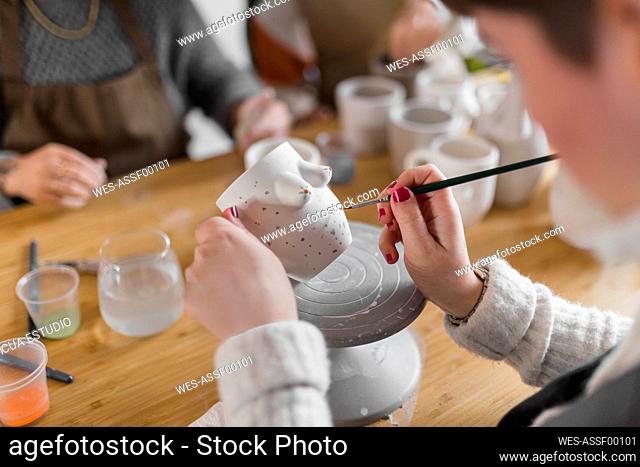 Female artist painting cup with colleagues at workbench