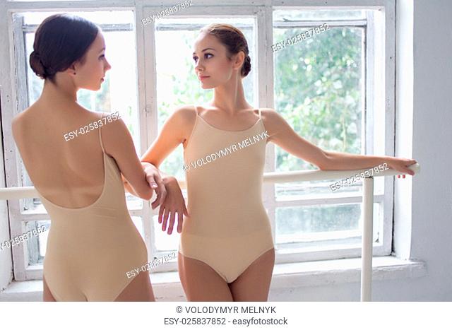 The two classic ballet dancers posing at ballet barre on a white room background