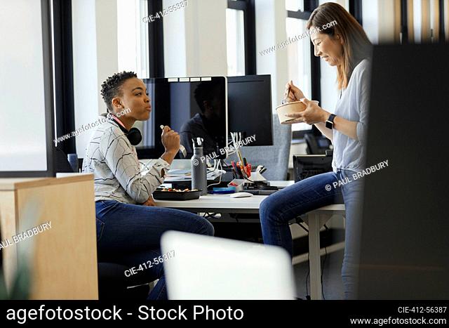 Businesswomen eating takeout lunch at desk in office