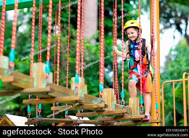 Child in forest adventure park. Kids climb on high rope trail. Agility and climbing outdoor amusement center for children