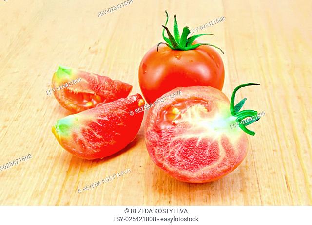 One whole tomato, half and two slices of tomato on the background of wooden boards