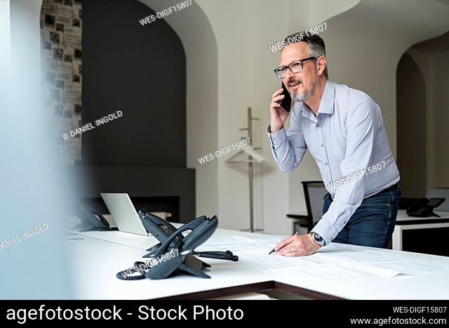 Businessman working while talking on mobile phone in office