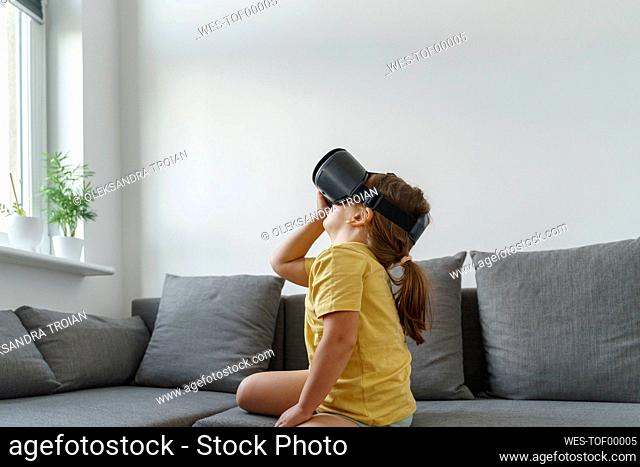 Girl wearing VR glasses sitting on sofa in living room