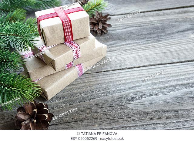 Christmas composition of pine cones, spruce branches and stack of gift boxes tied with red ribbons on the background of old unpainted wooden boards; with...