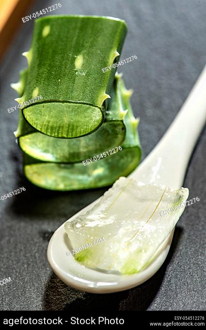 Aloe vera slices on dark background and spoon with aloe gel. Health and beauty concept. Closeup aloe pieces on backlight