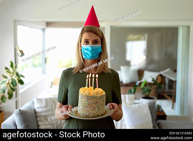 Portrait of woman wearing face mask holding a cake at home