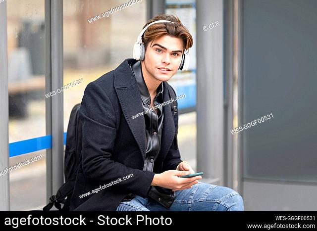 Handsome young man listening music while sitting at bus stop