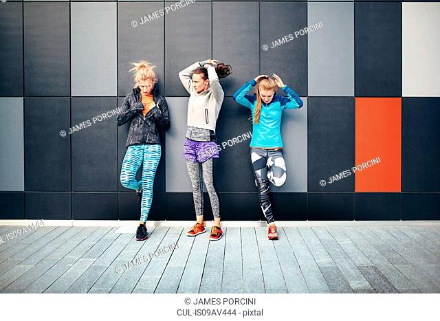 Three female runners putting up their hair in city underpass
