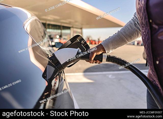 Hands of woman inserting plug into electric car
