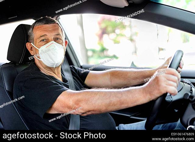Senior in his 70s driving a car wearing face mask for protection against corona virus