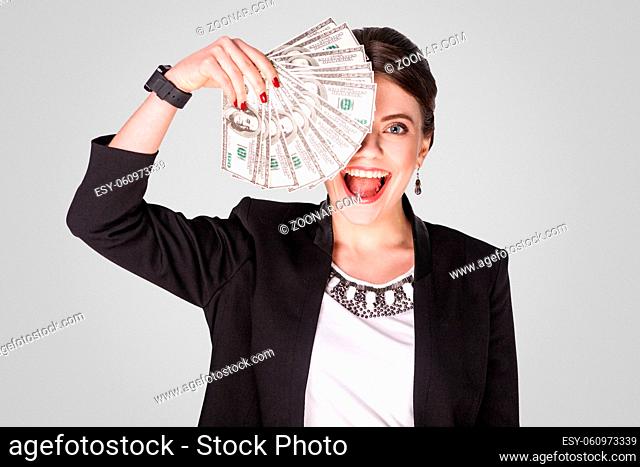Businesswoman showing at cash, dollar and toothy smile. Studio shot, indoor. Isolated on grey background