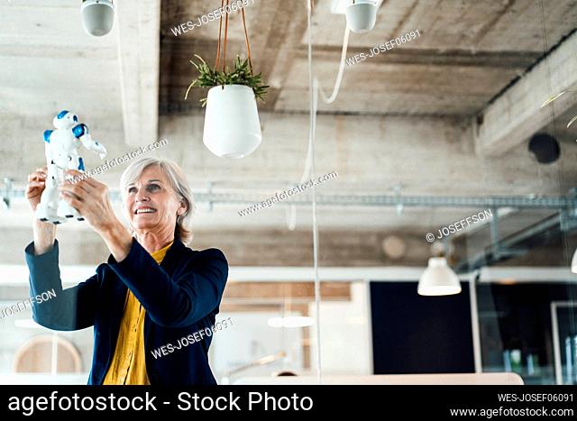 Smiling businesswoman holding robot at workplace