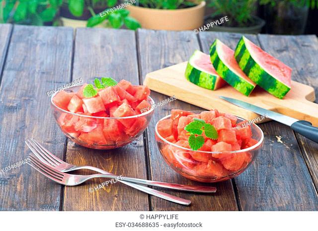 Watermelon cut in small cubes and served in two glas dishes on wooden table in rustic style