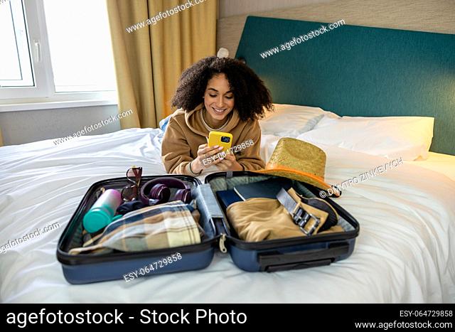 Ready for vacation. Curly-haired pretty young woman packing her suitcase