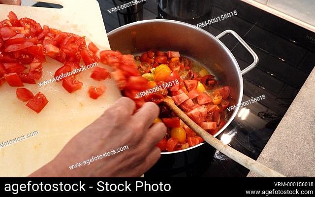 A woman at home chops tomatoes for a pasta sauce