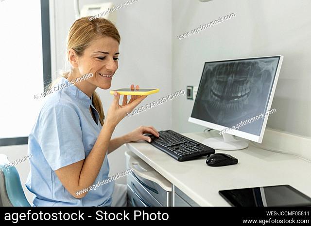Smiling dentist talking on mobile phone through speaker at dental clinic