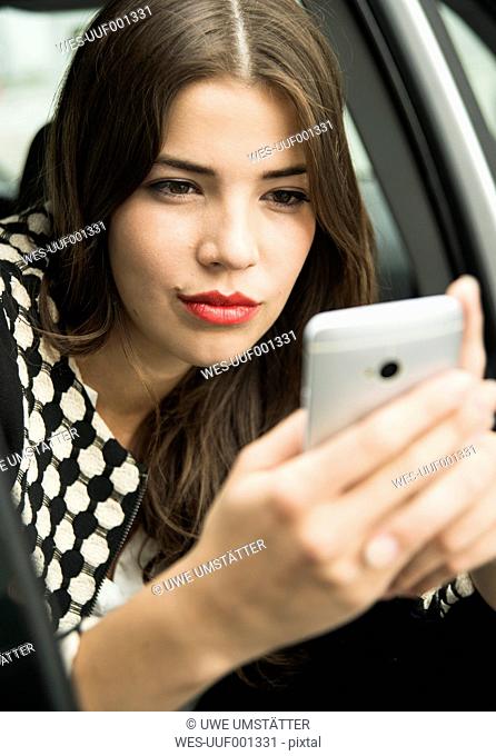 Portrait of young woman sitting in car taking a selfie with her smartphone