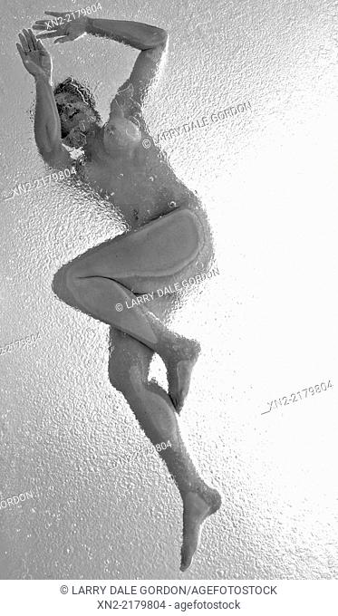 Nude woman on glass table under spotlight with falling rain, black and white shot from below