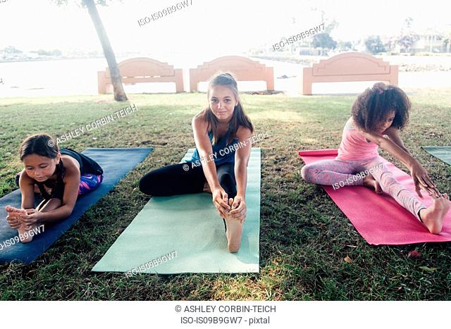 Three schoolgirls practicing yoga pose on school sports field