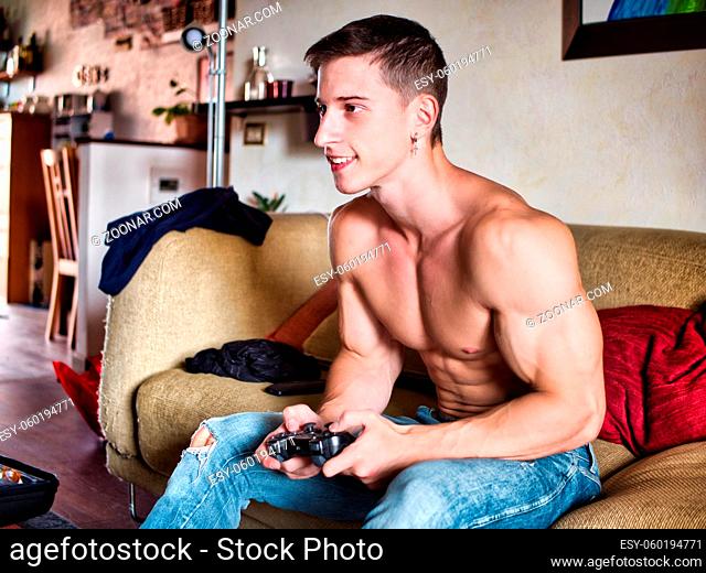 Young shirtless man playinig videogame smartphone at home while sitting on a couch