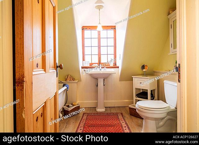 Freestanding roll top bathtub, pedestal sink and toilet in upstairs bathroom with faded pinewood floorboards inside an old renovated 1650s house, Quebec, Canada